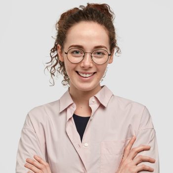 attractive-european-girl-with-charming-smile-keeps-arms-folded-wears-round-spectacles